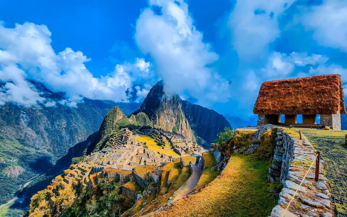 Terraced ruins of Machu Picchu below a cloud-capped peak, with a thatched stone hut on the right