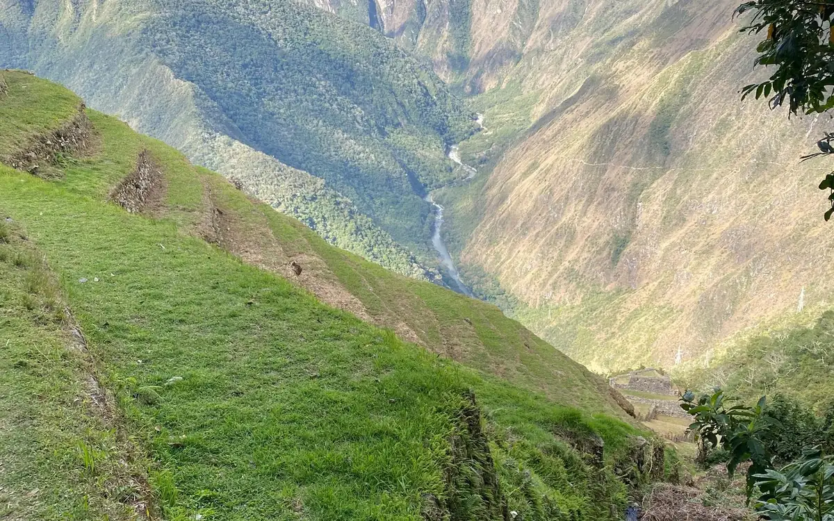 A narrow grassy terrace running along a steep slope high above a river valley