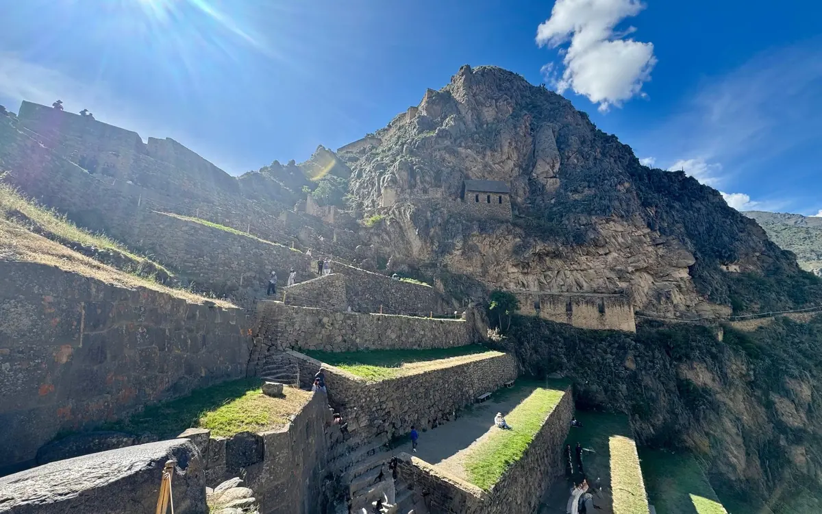 Grasbewachsene Steinterrassen unter einem felsigen Gipfel in Ollantaytambo