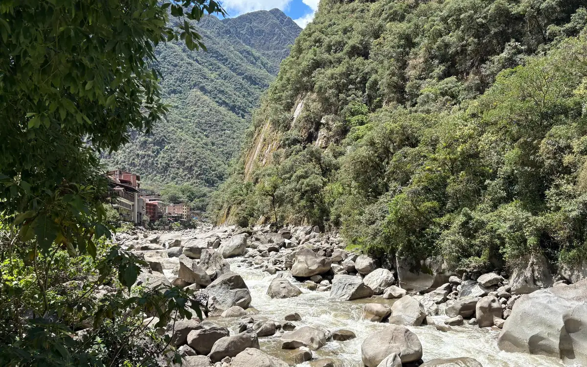 A boulder-filled river between steep green slopes, with tall buildings upstream