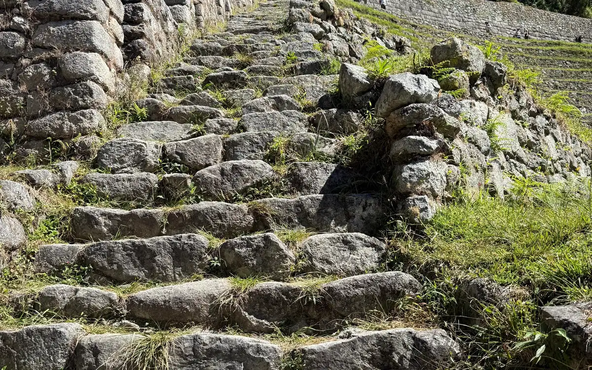 Marches de pierre usées gravissant une pente verte entre des murs de pierre
