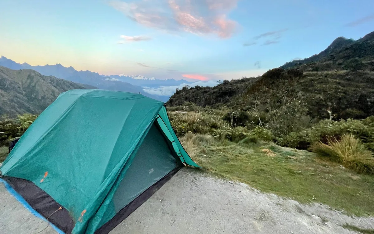 A green dome tent on a gravel pitch at dusk with distant snowy peaks